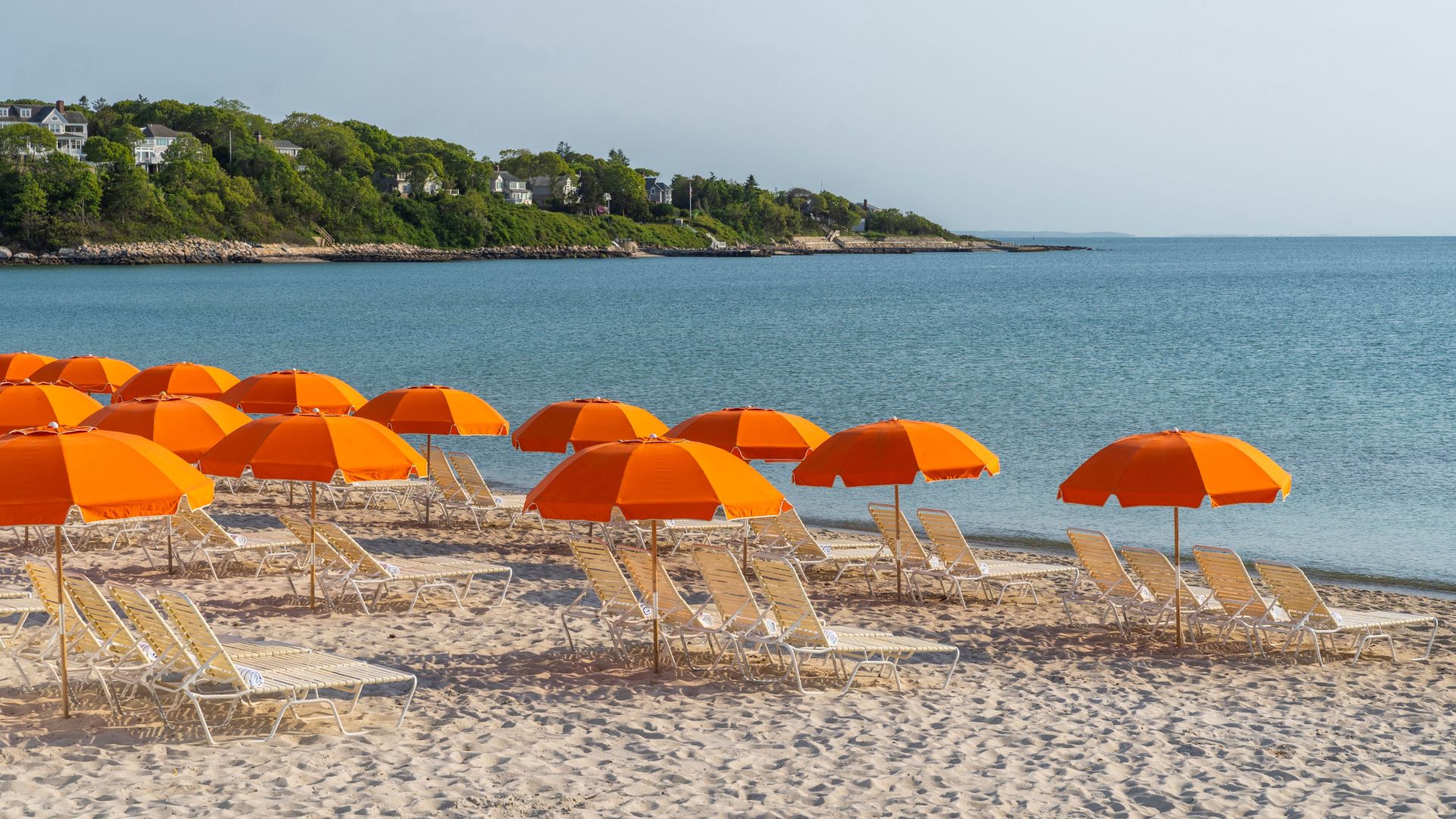 A Row Of Beach Chairs And An Orange Umbrella