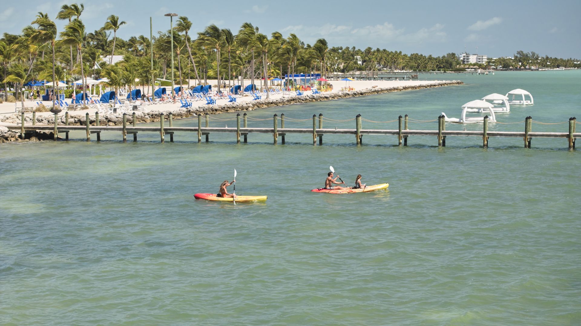 A Couple Of People In Kayaks In A Body Of Water By A Dock And A Beach